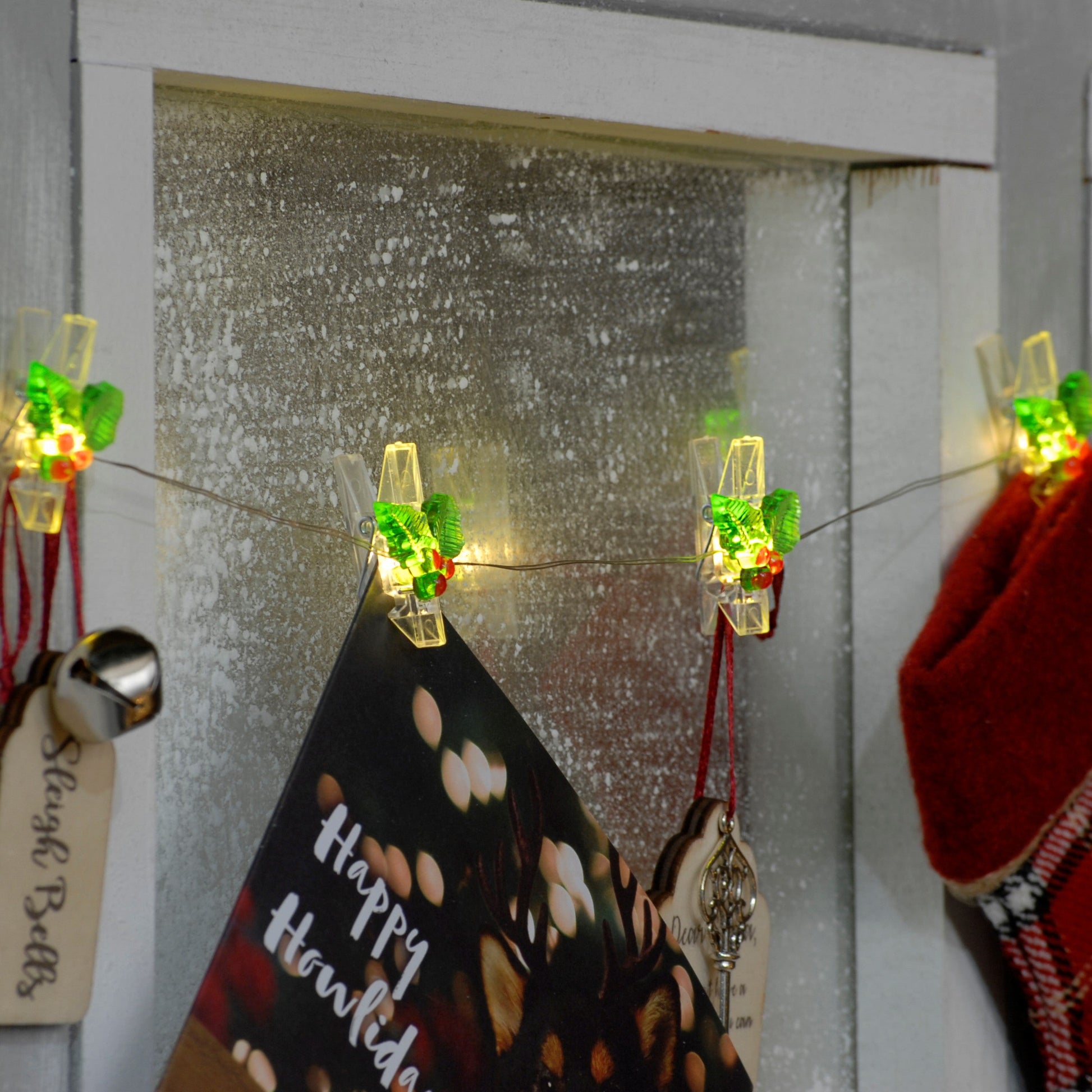 Holly design peg led lights shown hanging on a wall with stocking and cards and other Christmas objects hanging from the pegs