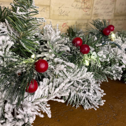 close up image of green foliage berry LED lights, that have been entwined in a snowy Christmas garland