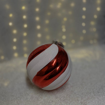 Red shiny and white glitter striped bauble with a silver wire placed on top of white snow with a warm warm led strands blurred background