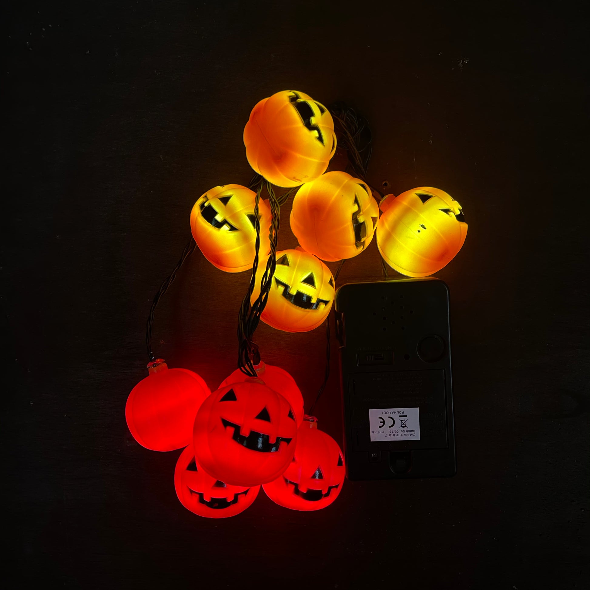 Orange LED pumpkin lights clumped together on a plain backgroud next to the battery box to show of the lights clearer